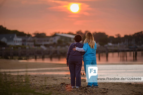 Frau und Pflegerin genießen den Sonnenuntergang am Abend am Meer