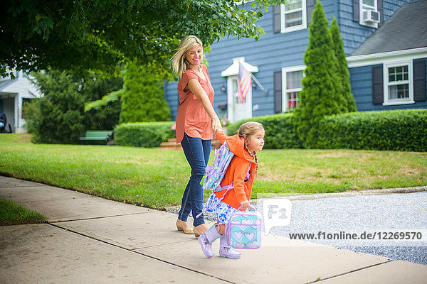 Mid adult woman walking with eager daughter on suburban sidewalk