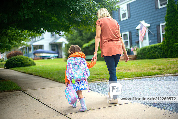 Mid adult woman walking with daughter on suburban sidewalk  rear view