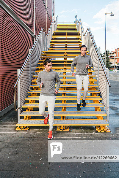 Junge erwachsene männliche Zwillinge laufen zusammen  laufen die Stadttreppe hinunter