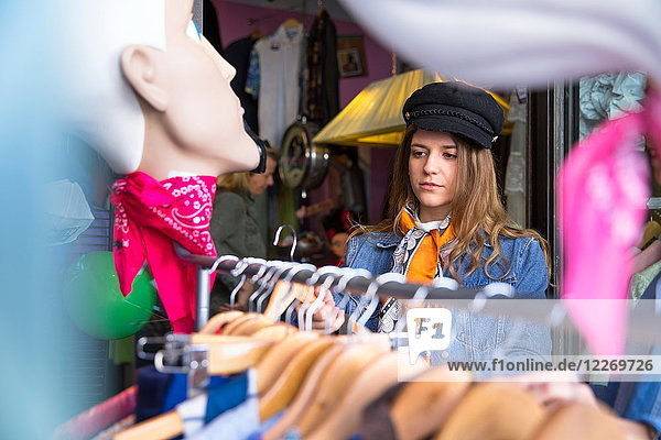 Junge Frau stöbert in einem Secondhand-Laden nach Vintage-Kleidung