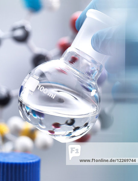 Wissenschaftler bereitet während eines Experiments chemische Formeln in einem Laborkolben vor  im Hintergrund ein Molekularmodell