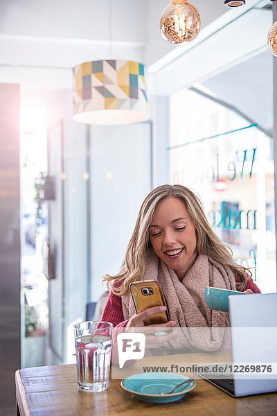 Frau sitzt im Café  schaut auf Smartphone  hält Kaffeetasse