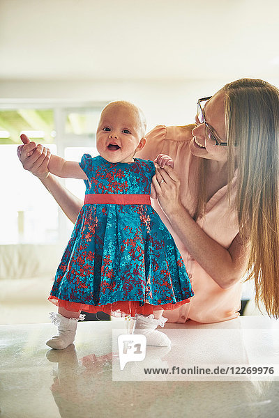 Frau hält Händchen mit Baby-Tochter auf Tisch stehend  Porträt