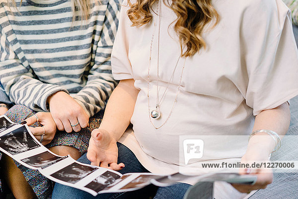 Schwangere und Freundin auf dem Sofa beim Betrachten des Ultraschallbildes  ausgeschnitten