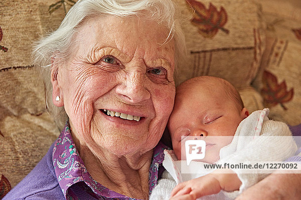 Ältere Frau wiegt Baby Urenkelin auf Sessel  Portrait