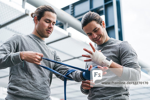 Identische männliche erwachsene Zwillingsboxer trainieren im Freien  bandagieren die Hände mit Handtuch