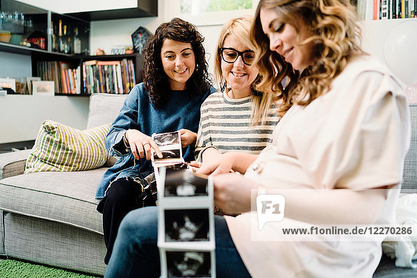 Schwangere und Freundinnen auf dem Sofa beim Betrachten von Ultraschallbildern