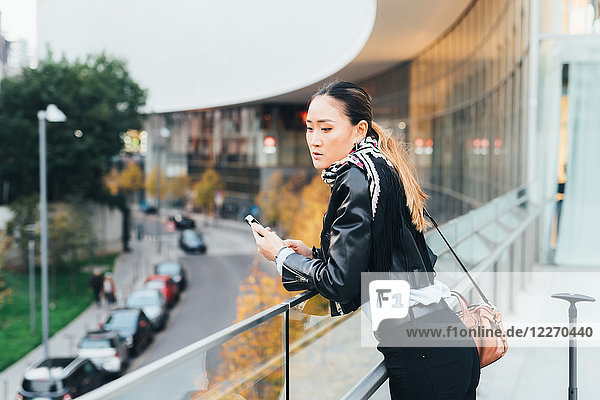 Woman  outdoors  leaning on railings  holding smartphone