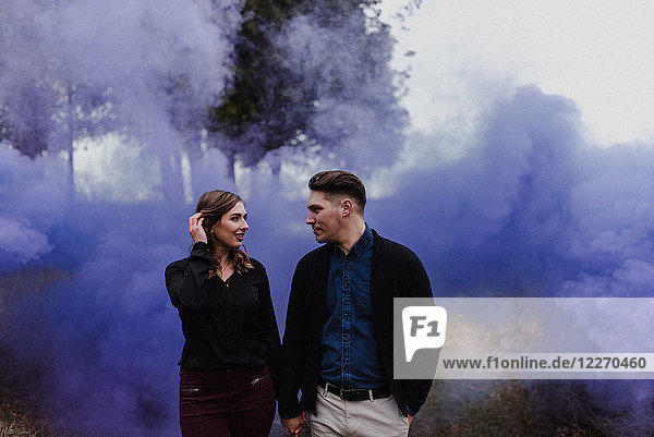 Junges Paar hält sich an blauer Rauchwolke an den Händen