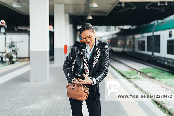Woman walking along train platform  going through bag  using smartphone