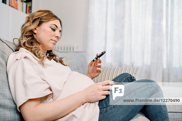 Schwangere Frau auf dem Sofa betrachtet Blutzuckertestergebnis