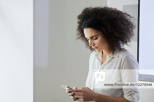 Geschäftsfrau im Büro textet auf Smartphone