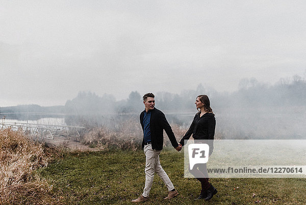Junges Paar hält sich beim Gehen auf nebligem Grasland an den Händen,  Ottawa,  Kanada