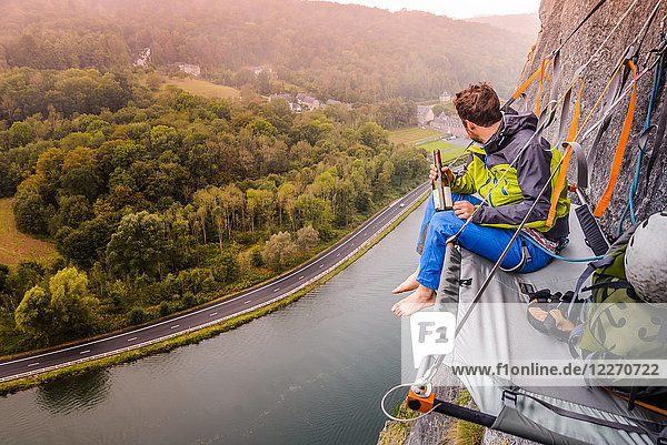 Junger männlicher Bergsteiger sitzend Felswand portaledge über der Maas  Freyr  Belgien  erhöhte Ansicht