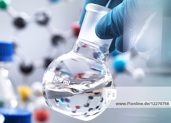 Wissenschaftler bereitet während eines Experiments chemische Formeln in einem Laborkolben vor  im Hintergrund ein Molekularmodell