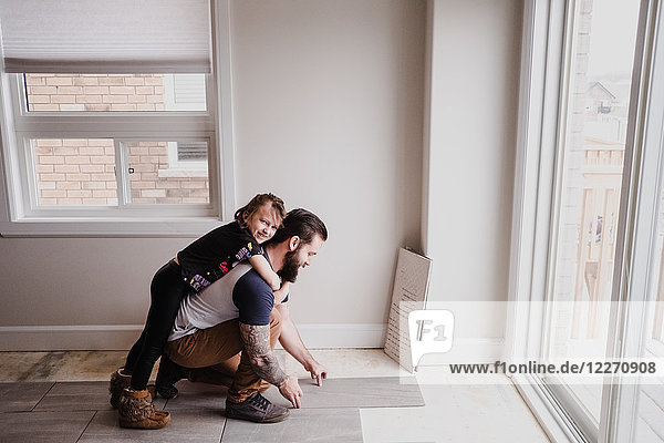 Mädchen umarmt Vater beim Verlegen von Bodenfliesen