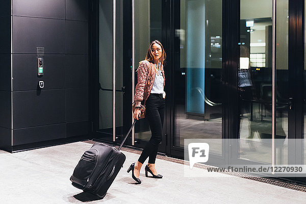 Woman walking towards hotel  pulling wheeled suitcase  looking over shoulder