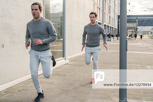 Young adult male twin runners  running along city sidewalk