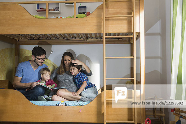 Vater und die schwangere Mutter lesen ihren beiden Söhnen auf dem Etagenbett ein Buch vor  München  Deutschland