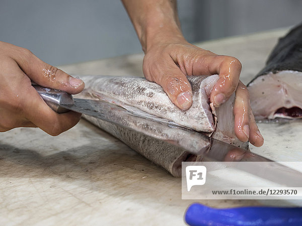 Mann schneidet Fisch mit Messer