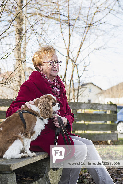 Alte Frau und ihr Hund sitzen draußen auf einer Bank