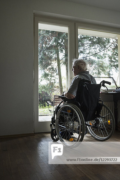 Älterer Mann im Rollstuhl schaut durch ein Fenster hinaus
