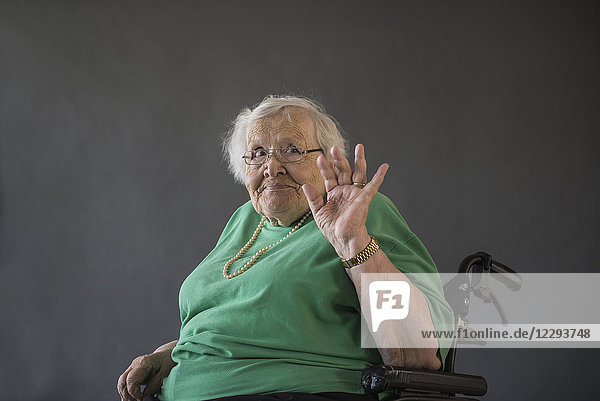 Porträt einer älteren Frau  die im Rollstuhl sitzt und mit der Hand winkt