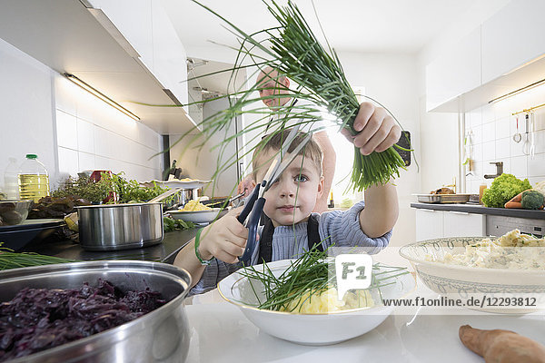Kleiner Junge schneidet frischen Bio-Schnittlauch in der Küche