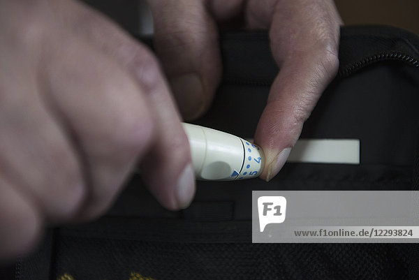 Senior man using pen-like lancing device to prick finger