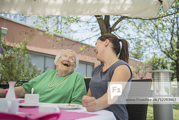 Ältere Frau lacht mit Krankenschwester im Pflegeheim