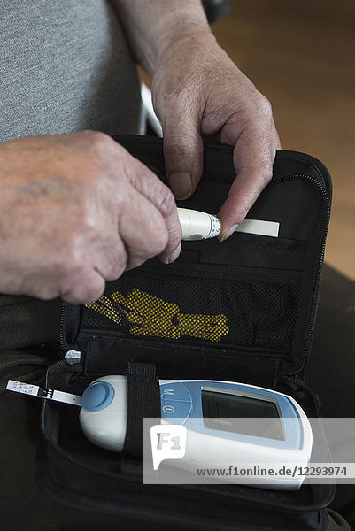 Senior man using pen-like lancing device to prick finger