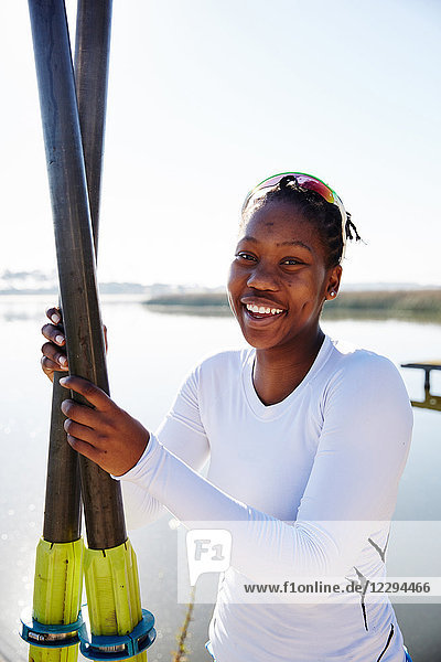 Portrait lächelnde  selbstbewusste Rudererin mit Rudern am sonnigen Seeufer