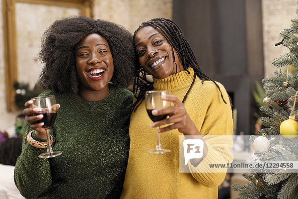 Portrait smiling  happy mother and daughter drinking wine next to Christmas tree