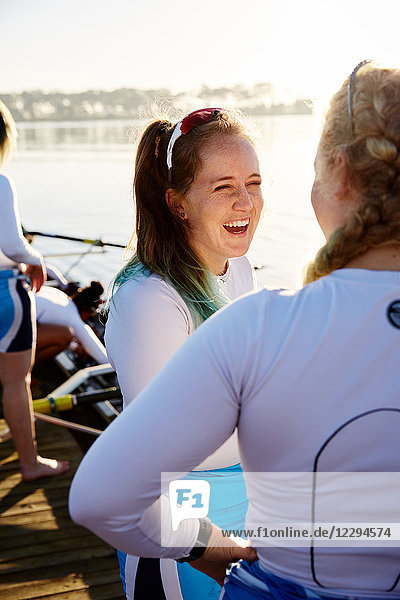 Female rowers smiling and talking at sunny lakeside