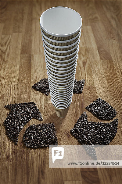 Coffee beans forming recycle symbol around stack of recyclable coffee cups