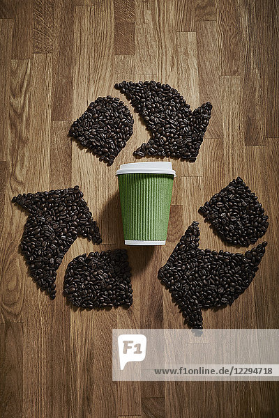 Coffee beans forming recycle symbol around green recyclable coffee cup