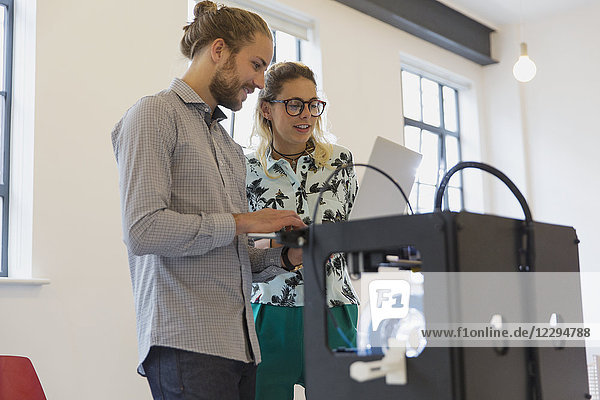 Designer mit Laptop neben 3D-Drucker im Büro