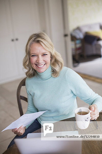 Portrait smiling confident female freelancer working at laptop and drinking tea at home