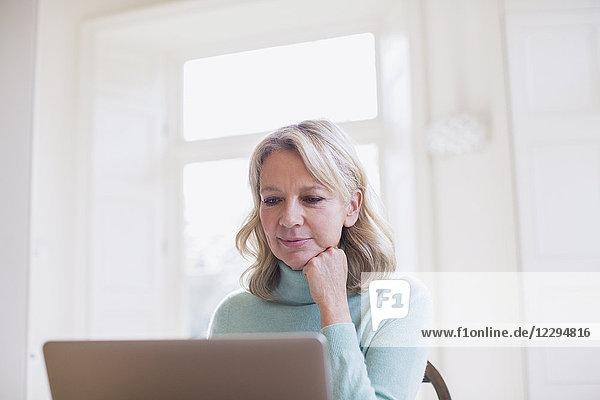 Focused mature female freelancer working at laptop at home