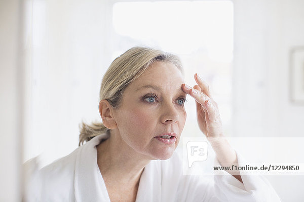 Reife Frau berührt Augenbraue im Badezimmerspiegel
