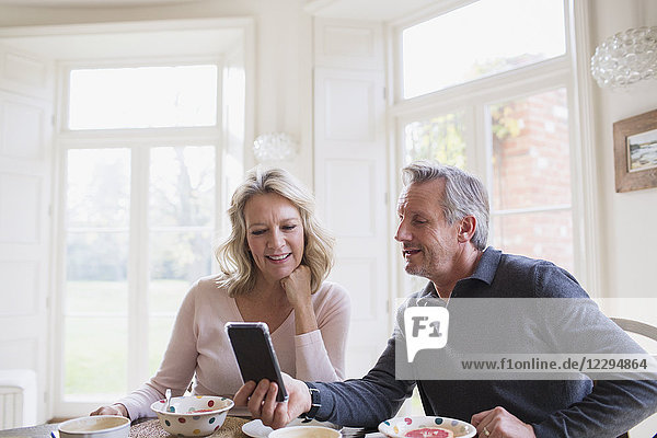 Mature couple using smart phone at breakfast table