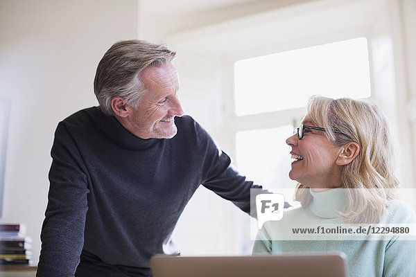 Smiling mature couple talking at laptop