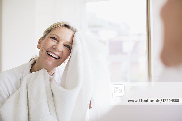 Smiling mature woman drying face with towel at bathroom mirror