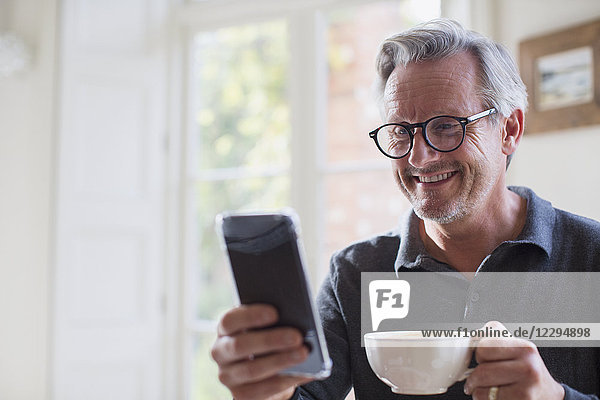 Lächelnder reifer Mann  der Tee trinkt und sein Smartphone benutzt