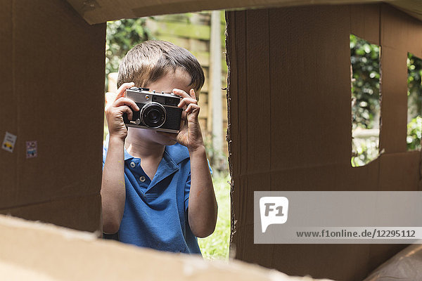 Junge fotografiert durch Pappspielhaus im Hinterhof