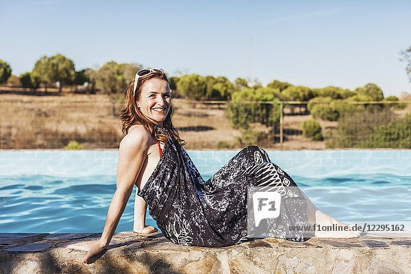 Seitenansicht Porträt einer lächelnden erwachsenen Frau mit Sarong am Pool an einem sonnigen Tag.