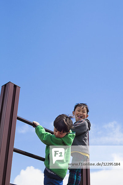 Flachwinkelansicht von Jungen  die auf Spielplatzgeräten gegen den blauen Himmel klettern.