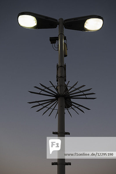 Low angle view of illuminated street light and surveillance cameras against sky