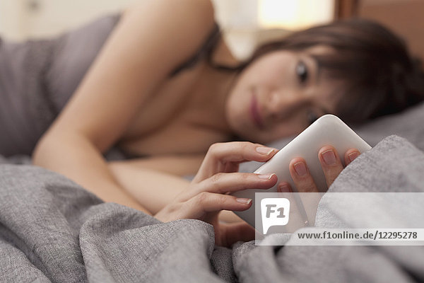 Junge Frau  die das Handy benutzt  während sie zu Hause auf dem Bett liegt.
